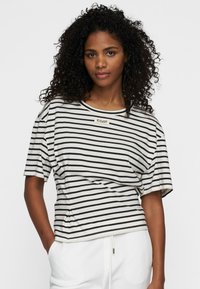 T-shirt a righe a maniche corte in tessuto crema e nero, con scollatura rotonda e un'etichetta sul petto, dal taglio rilassato.
