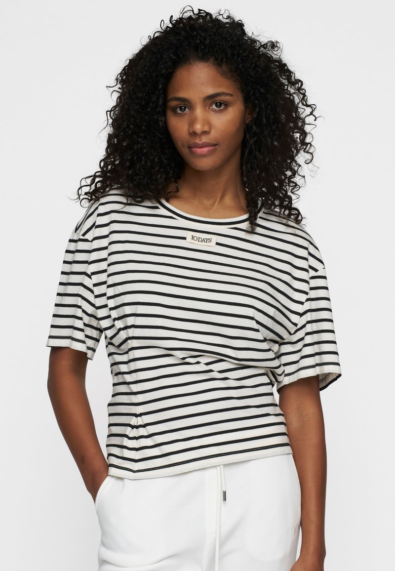 T-shirt a righe a maniche corte in tessuto crema e nero, con scollatura rotonda e un'etichetta sul petto, dal taglio rilassato.