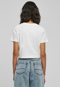 Hvit avkortet t-skjorte med korte ermer, med rund hals. Kombinert med høyt liv, falmede blå denimjeans med to baklommer.