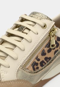 Beige sneakers with textured gold accents, leopard print detailing, and a side zipper. Features flat laces and a cushioned sole.