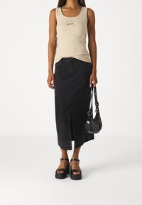 Débardeur beige avec un petit logo, associé à une jupe midi en denim noir, des sandales plateformes noires et un petit sac à bandoulière noir.