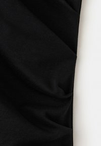 Tissu noir drapé avec plis visibles et texture sur fond blanc.