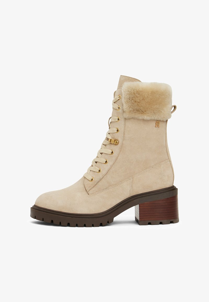 Botines de ante beige con un collar de piel sintética, ojales dorados y un tacón marrón grueso; cuenta con una suela de goma con relieve para mayor agarre.