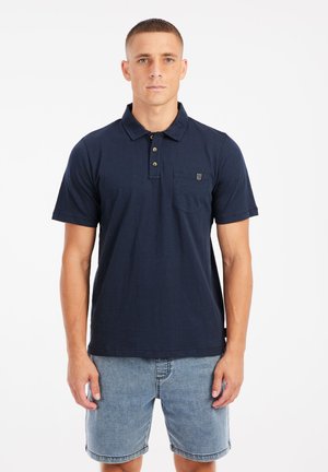 Marineblauwe polo met een klassieke kraag, drie knoopsluitingen, korte mouwen en een borstzakje. De stof lijkt zacht en ademend te zijn.