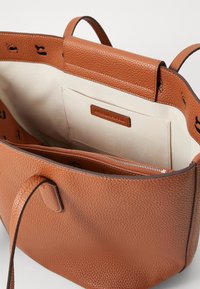 Sac fourre-tout en cuir tan avec une finition texturée, dotée d'un compartiment avec fermeture éclair et d'un intérieur beige, équipé de deux poignées robustes.