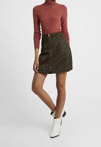 Top dolce a collo alto color ruggine abbinato a una mini gonna nera con stampa leopardata e cerniera frontale. Modella con stivaletti bianchi alla caviglia.