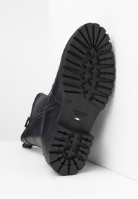 Bottines en cuir noir avec une semelle en caoutchouc texturé, fermeture éclair sur le côté et logo embossé sur la semelle. Taille 37 indiquée.