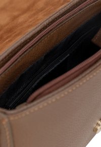 Interno di una borsa a tracolla in pelle marrone con fodera in tessuto nero, dotato di una tasca con zip e dettagli in morbido marrone.