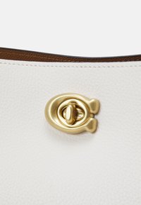 Bílá kožená kabelka s výrazným zlatým kováním, hladkým povrchem a kontrastní hnědou podšívkou.