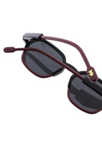 Sunglasses med bordeauxfärgade plastbågar och mörkt tonade linser. Har en distinkt svart bro och en guldfärgad logotypaccent på skalmen.