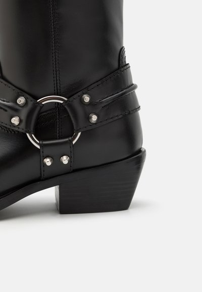 Stivali alla caviglia in pelle nera con un accento in argento a forma di anello rotondo e due cinturini orizzontali con dettagli a pressione, montati su un tacco in legno chunk.