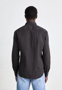 Temno srajca s kraguljem, dolgi rokavi, ovratnik, bombažni material, minimalističen dizajn, gladka tekstura, v kombinaciji z svetlim denim hlačami.