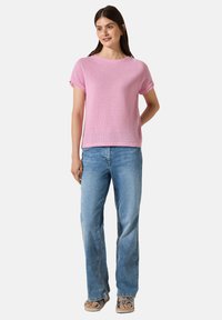 Haut en tricot rose à manches courtes, col rond et coupe ample, associé à un jean large bleu clair et des sandales beiges.