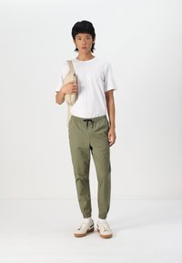 Casual outfit bestaande uit een wit T-shirt, olijfgroene joggerpants met een elastische tailleband en beige sneakers met een structuurzool.