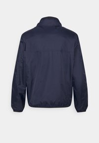 Giacca a vento navy, leggera, texture liscia, con colletto rialzato e polsini elasticizzati. Presenta un yoke sulla schiena e nessun marchio visibile.
