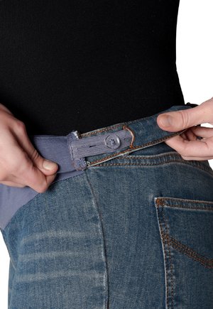 Jean en denim avec une taille élastique bleue, montrant une main ajustant la ceinture. Surpiqûres visibles de couleur marron clair. Texture douce et lisse.