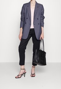 Blazer grigio doppiopetto su top rosa, abbinato a pantaloni neri a sigaretta e décolleté neri con cinturini. Borsa nera con design circolare.