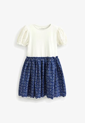 Robe à manches courtes avec un haut blanc et une jupe bleu marine ornée de motifs floraux blancs. La jupe présente des détails froncés et un ourlet en forme de scallop.