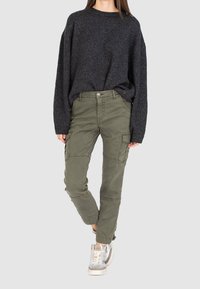 Tmavě šedý pletený svetr s volným střihem, doplněný olivově zelenými cargo kalhotami s bočními kapsami a zúženým střihem nohavic. Stříbrné tenisky.