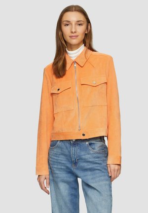 Afgekorte oranje corduroy jas met twee borstzakken, een metalen rits en een puntige kraag, gecombineerd met blauwe denim spijkerbroek.