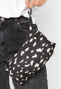Czarna torba materiałowa w białe nieregularne plamki, z zamkiem błyskawicznym i krótkim uchwytem. Torba wydaje się miękka i lekka.
