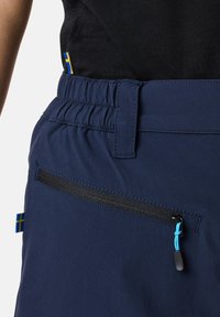 Marineblauwe shorts met een elastische tailleband, uitgerust met een ritszak en een blauwe trekstrip. Decoratieve Zweedse vlag tag aan de zijkant.