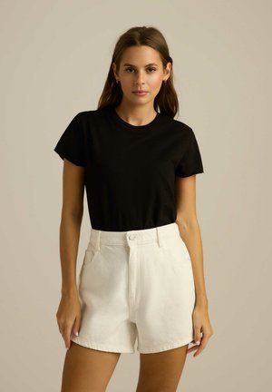 Czarna bawełniana koszulka zestawiona z białymi szortami dżinsowymi. Szorty mają wysoki stan, przednie kieszenie i zapięcie na guzik.