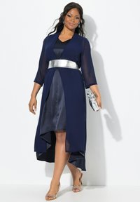 Marineblauw jurk met een zilveren riem, lange doorschijnende mouwen en een asymmetrische zoom. Heeft een gladde satijnachtige textuur en een subtiele glans.