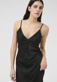 Crna saten haljina s bešivenim korzetom s cvjetnim uzorcima, tankim naramenicama i središnjim gumbom. Glatka tekstura i elegantan dizajn.