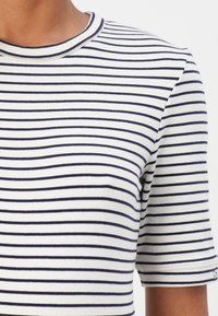 Gestreept t-shirt in beige en marineblauw, met korte mouwen en een ronde halslijn. De stof lijkt zacht, met een gladde textuur en gelijkmatige strepen.