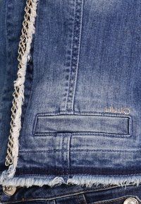 Jeansjacka med ljusblått tyg, fransat såll, silverkedjeinslag framtill och en bakficka med ett guldlogotyp.