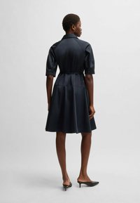 Navy blue shirt dress with short sleeves, a fitted waist, and flared skirt. Smooth texture, collared neck, and cinched with a matching belt.