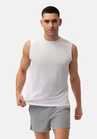 Weißes ärmelloses Sportshirt aus strukturierter Stoffqualität mit rundem Ausschnitt, kombiniert mit hellgrauen Shorts. Dezent platziertes Logo auf dem Shirt.