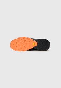 Podplat čevlja z oranžnim vzorcem spredaj in črnim vzorcem na peti, s logotipom Vibram v središču.