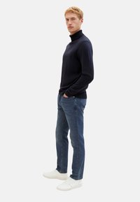 Maglione a dolcevita navy, materiale morbido, design aderente. Abbinato a jeans blu skinny e sneakers bianche. Stile minimalista.
