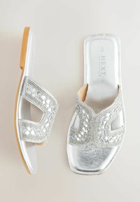 Sandales plates argentées avec orteils carrés ouverts, brides supérieures décoratives ornées de perles, et semelles de couleur beige, vues de dessus et de côté.