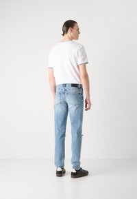 Hvit kortermet t-skjorte med svart kant, lys blå slitte jeans, og mørke sneakers med hvite detaljer, sett fra baksiden.