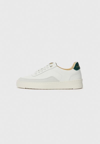 Zapatilla blanca con acentos de ante, puntera redondeada, cordones planos y suela de goma color crema. Presenta un logo verde en el talón.