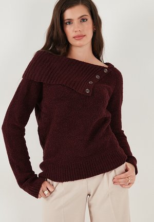 Burgunderfarbener Pullover mit asymmetrischem, geripptem Kragen, drei Knöpfen auf einer Seite und einem strukturierten, weichen Stoff. Mit langen Ärmeln und gerippten Bündchen.