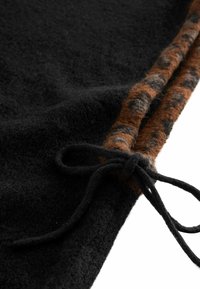 Fekete texturált szövet barna és fekete mintás díszítéssel az egyik szélén, fekete megkötött zsinórral.