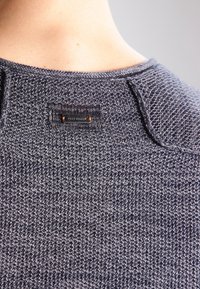 Gray knitted sweater with a textured pattern. Features a small brand label on the back and a round neck design. Soft fabric.