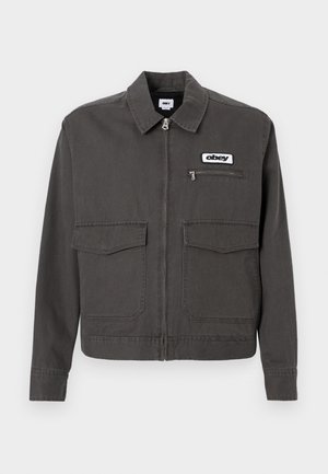 Σκούρο γκρι μπουφάν από βαμβάκι, με γιακά, κλείσιμο με φερμουάρ, δύο εμπρόσθιες τσέπες και ένα λογότυπο στο αριστερό στήθος.