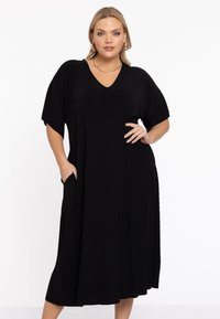 Robe noire côtelée avec un décolleté en V, des manches courtes et des poches latérales. Silhouette fluide, longueur genoux avec une texture douce.
