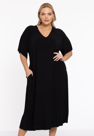 Zwarte, geribbelde jurk met een V-hals, korte mouwen en zijzakken. Vloeiende silhouet, knie-lengte met een zachte textuur.