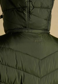 Zelená puffa bunda s kapucňou, s chevronovým prešívaním a decentným prémiovým vyšitím na chrbte. Hladká, lesklá textúra látky.