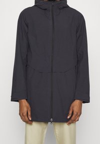 Tummansininen sadeviita, jossa on huppu, etuvetoketju ja kaksi sivutaskua. Kangas näyttää sileältä, ja se on hieman löysä, rento malli.