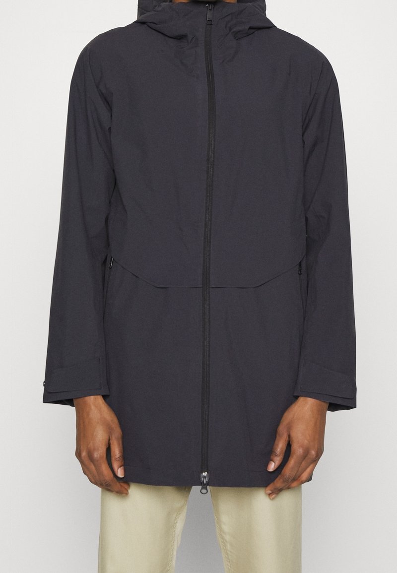 Tummansininen sadeviita, jossa on huppu, etuvetoketju ja kaksi sivutaskua. Kangas näyttää sileältä, ja se on hieman löysä, rento malli.