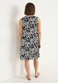 Ärmelloses Kleid in Schwarz und Weiß mit einem kräftigen, abstrakten Diamantmuster. Knielang, mit lockerem Schnitt und glattem Stoffgefühl.