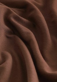 Bruine stof met een gladde textuur, met zachte plooien en een lichte, luchtige uitstraling, geschikt voor kleding of meubelbekleding.