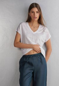 T-shirt bianco a scollo a V realizzato in tessuto leggero, abbinato a pantaloni larghi blu scuro con cintura elastica.